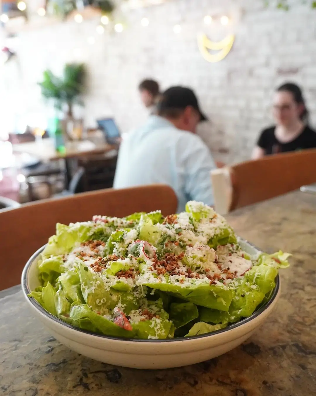 there is a bowl of salad on a table with people in the background