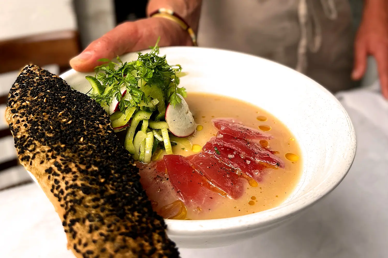 someone holding a bowl of soup with a piece of bread and a salad