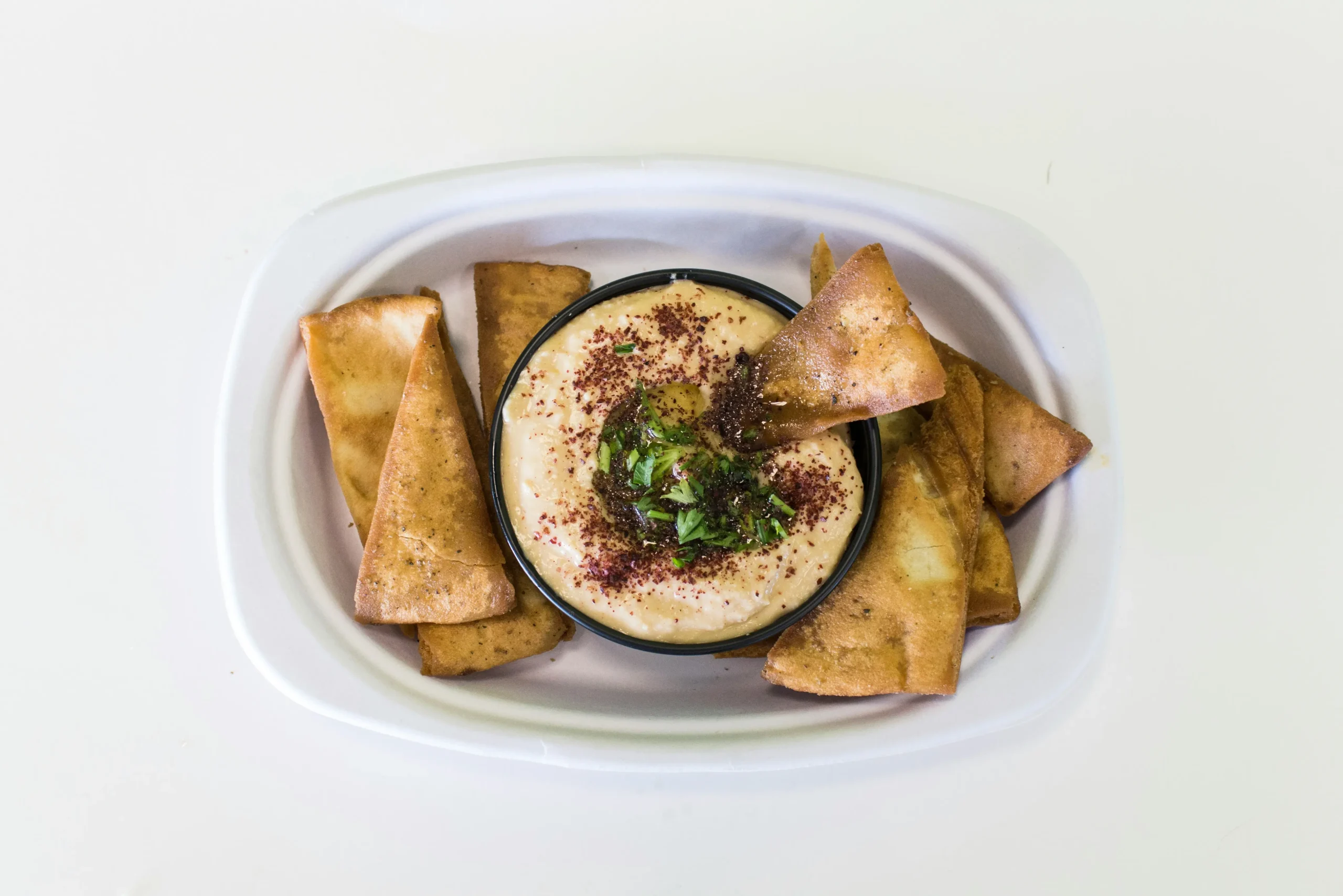 there is a bowl of dip and pita chips on a plate