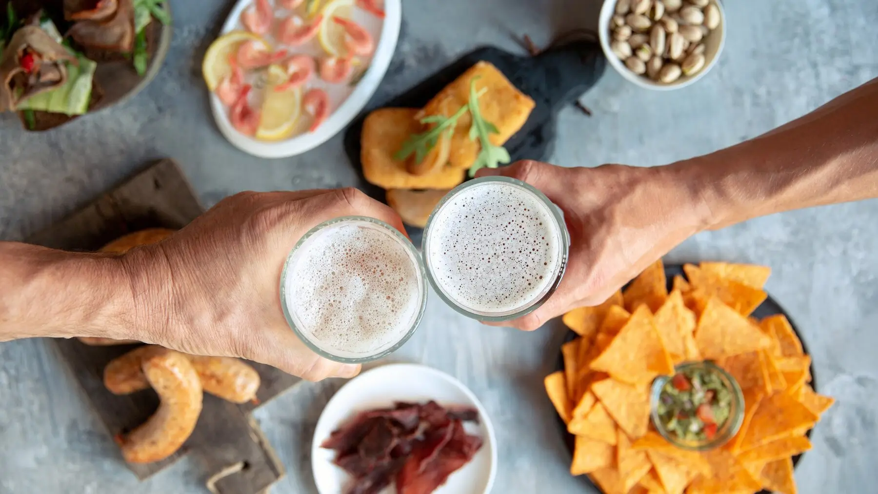 someone holding a glass of beer in front of a table with food
