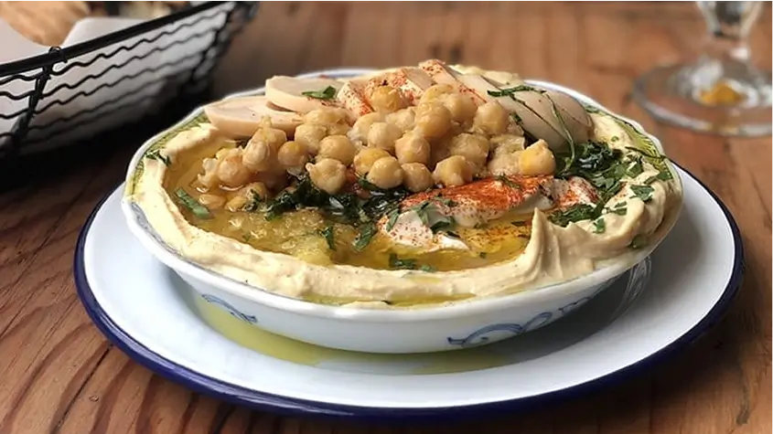 there is a bowl of hummusle with chickpeas and greens