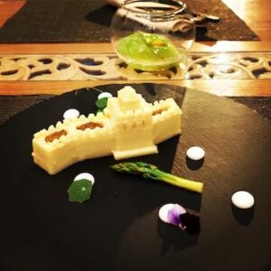 there is a black plate with a piece of cheese and asparagus on it