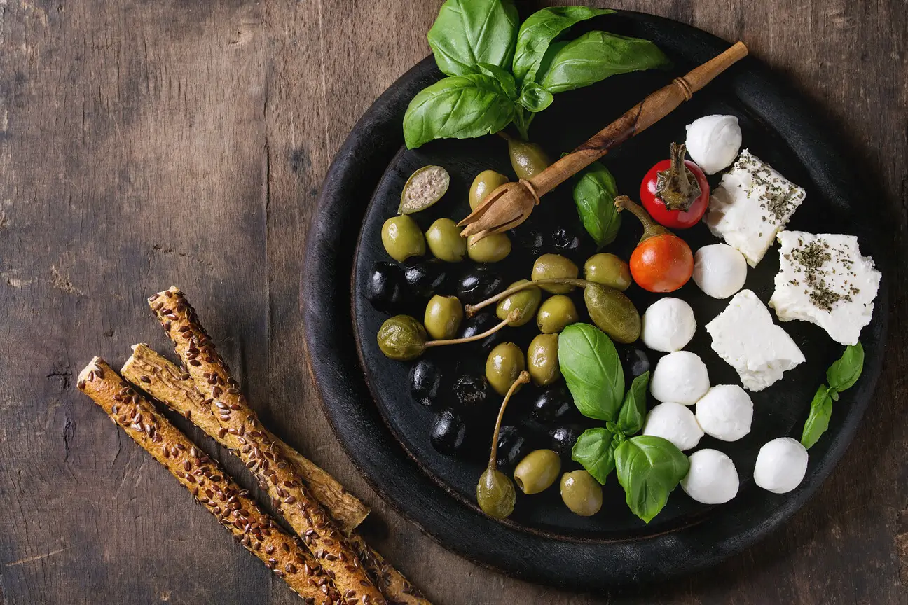 a close up of a plate of food with olives, cheese, and breadsticks