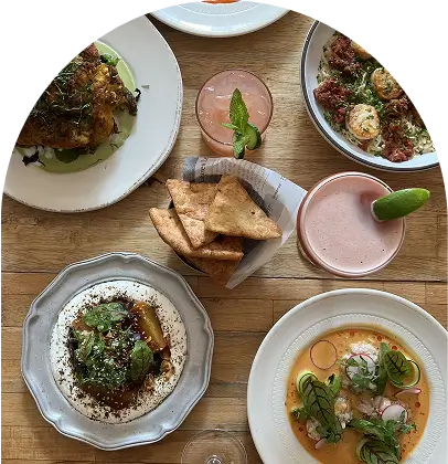 several plates of food are on a wooden table with drinks