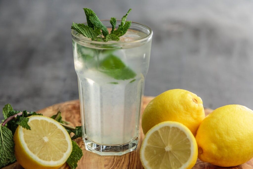there is a glass of lemonade and lemons on a cutting board