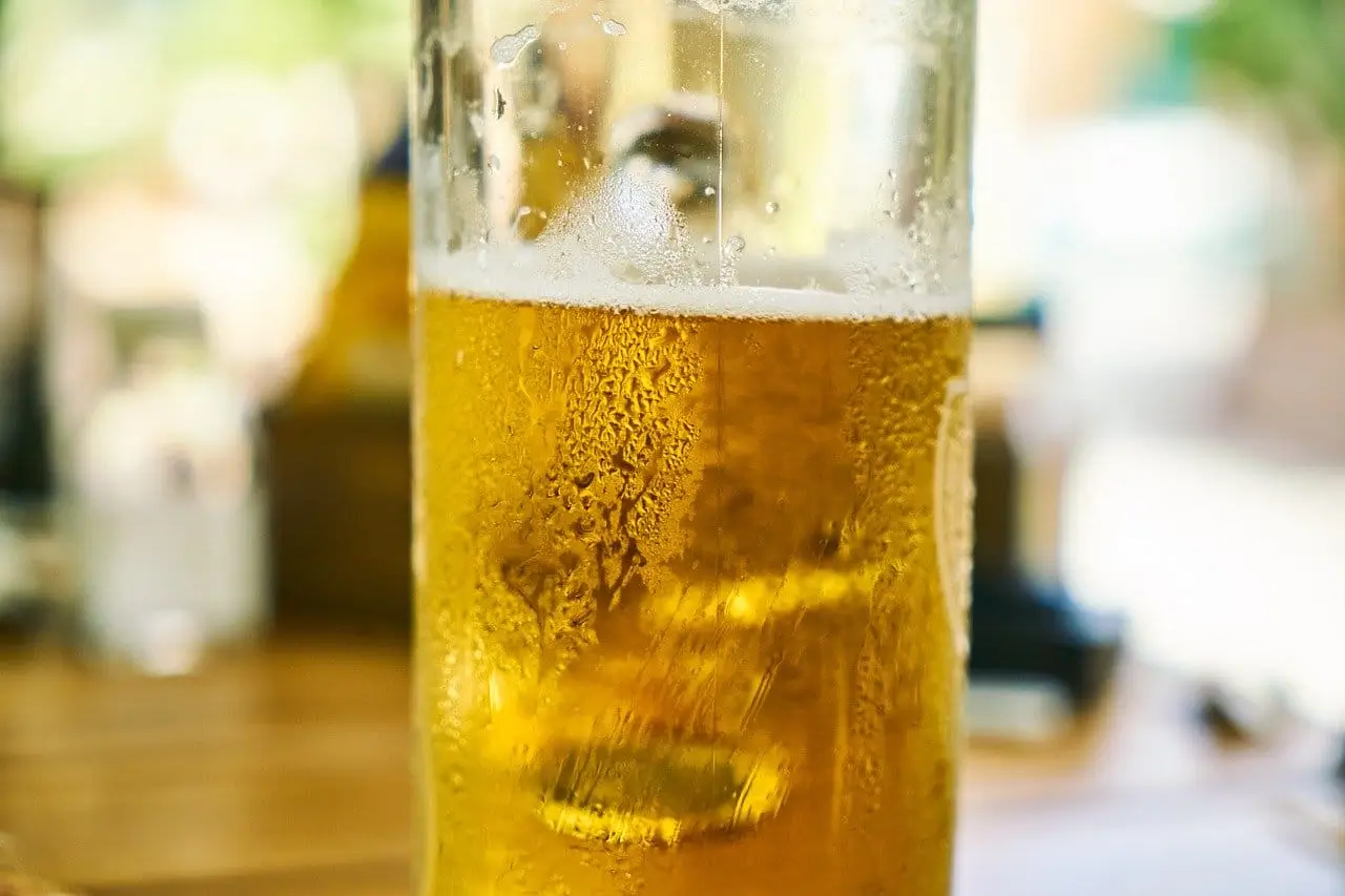 there is a glass of beer sitting on a table with a spoon