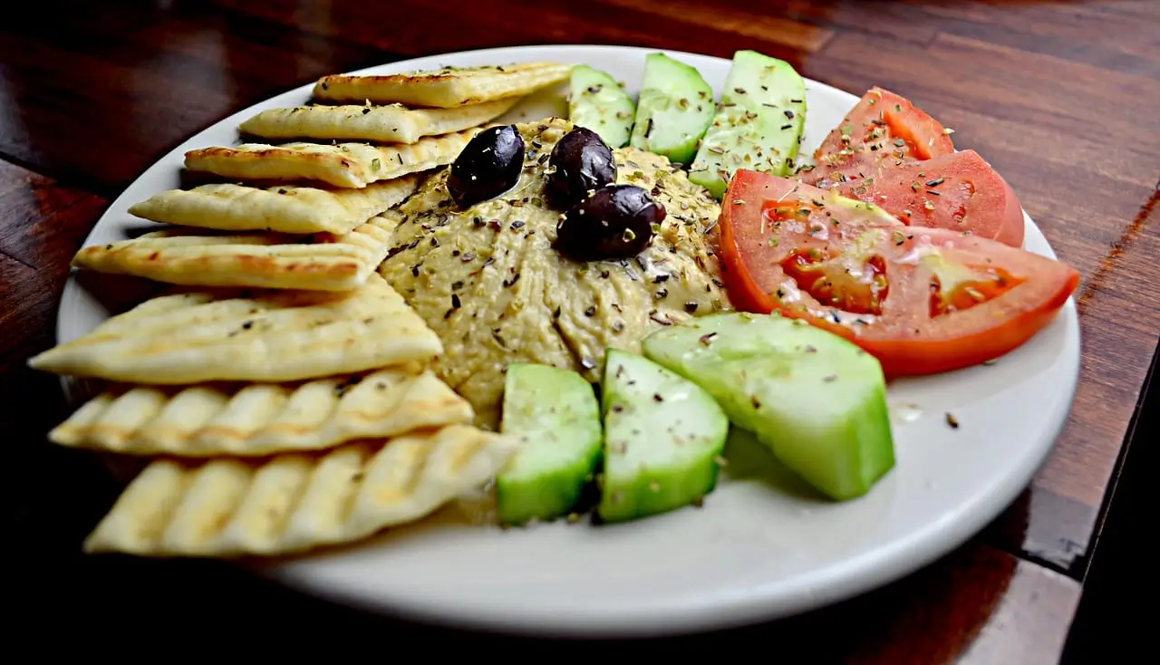 there is a plate of food with crackers, tomatoes, cucumbers, and olives