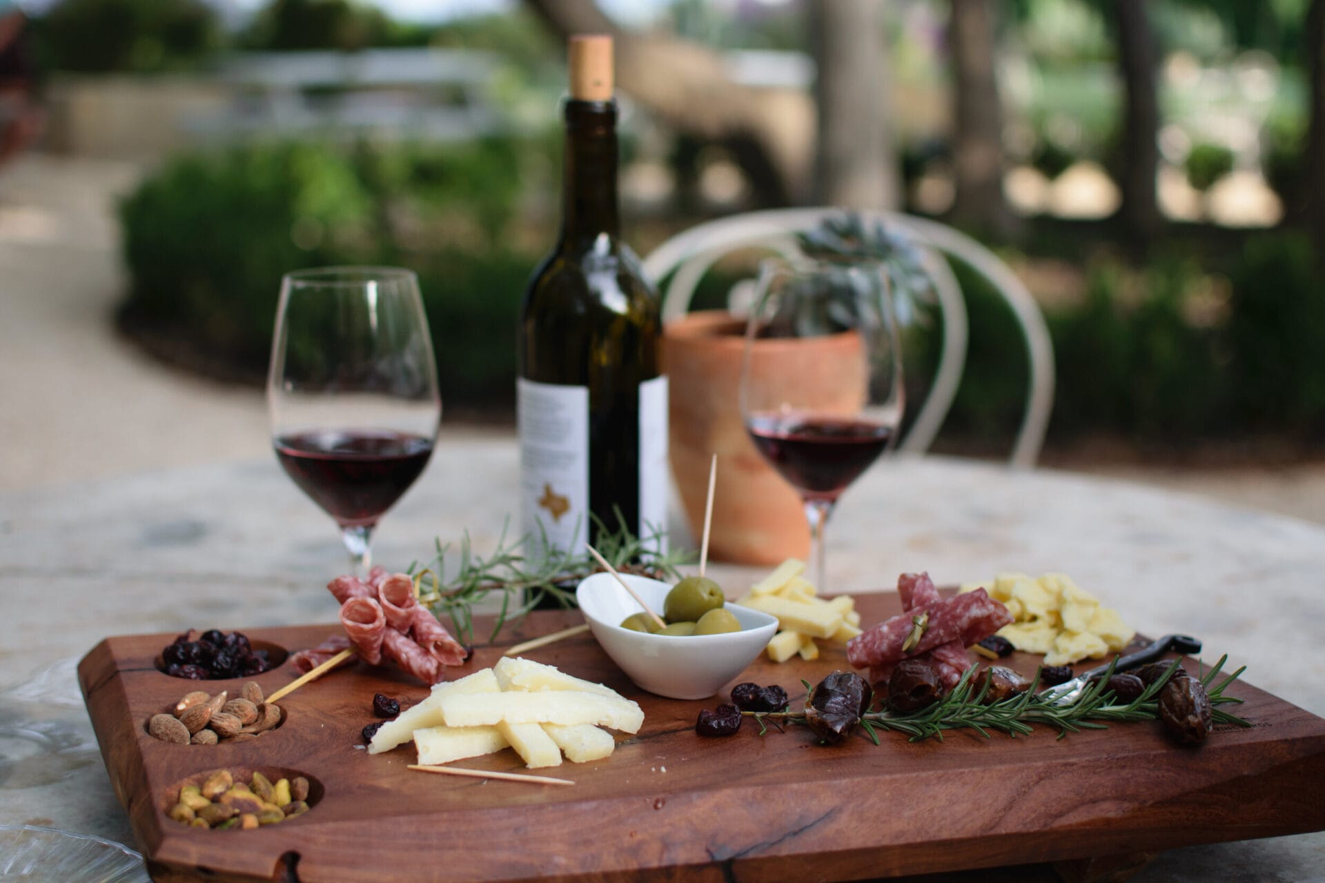 there is a wooden board with a cheese board, grapes, and olives