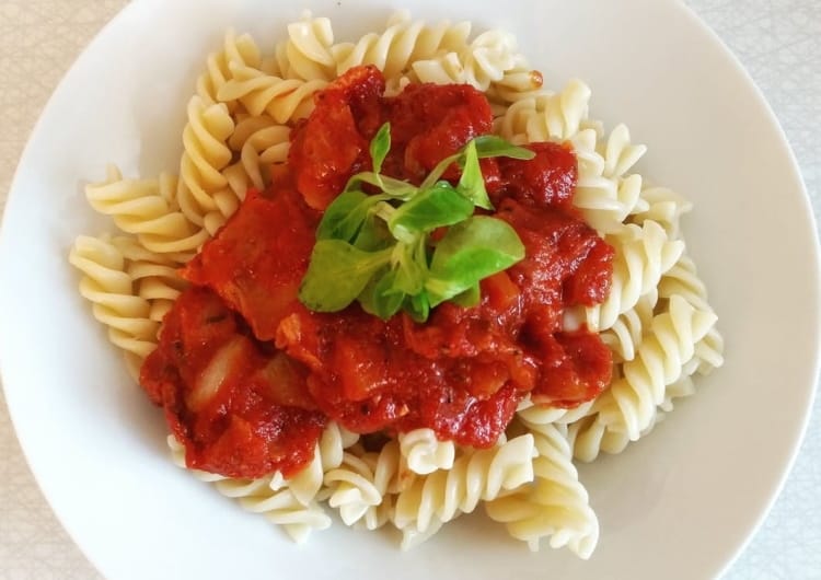a close up of a plate of pasta with sauce and a sprig of basil