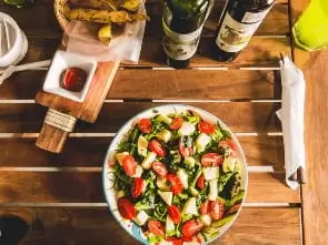 there is a bowl of salad on a wooden table with a bottle of wine