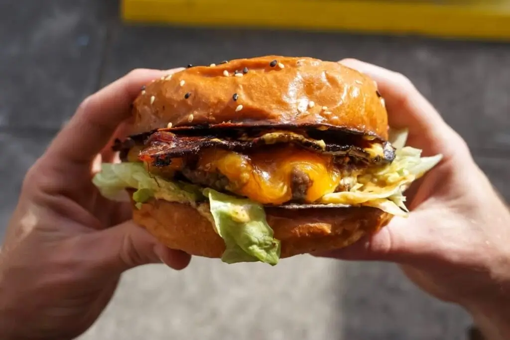 someone holding a large hamburger with bacon, lettuce, and cheese