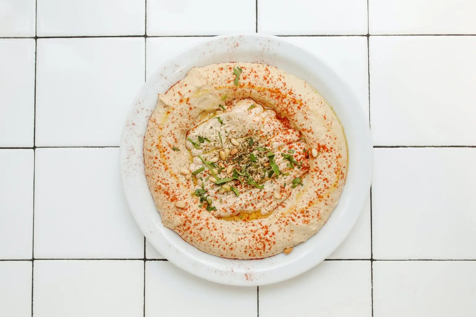 araffy hummusl with olive and herbs in a white bowl
