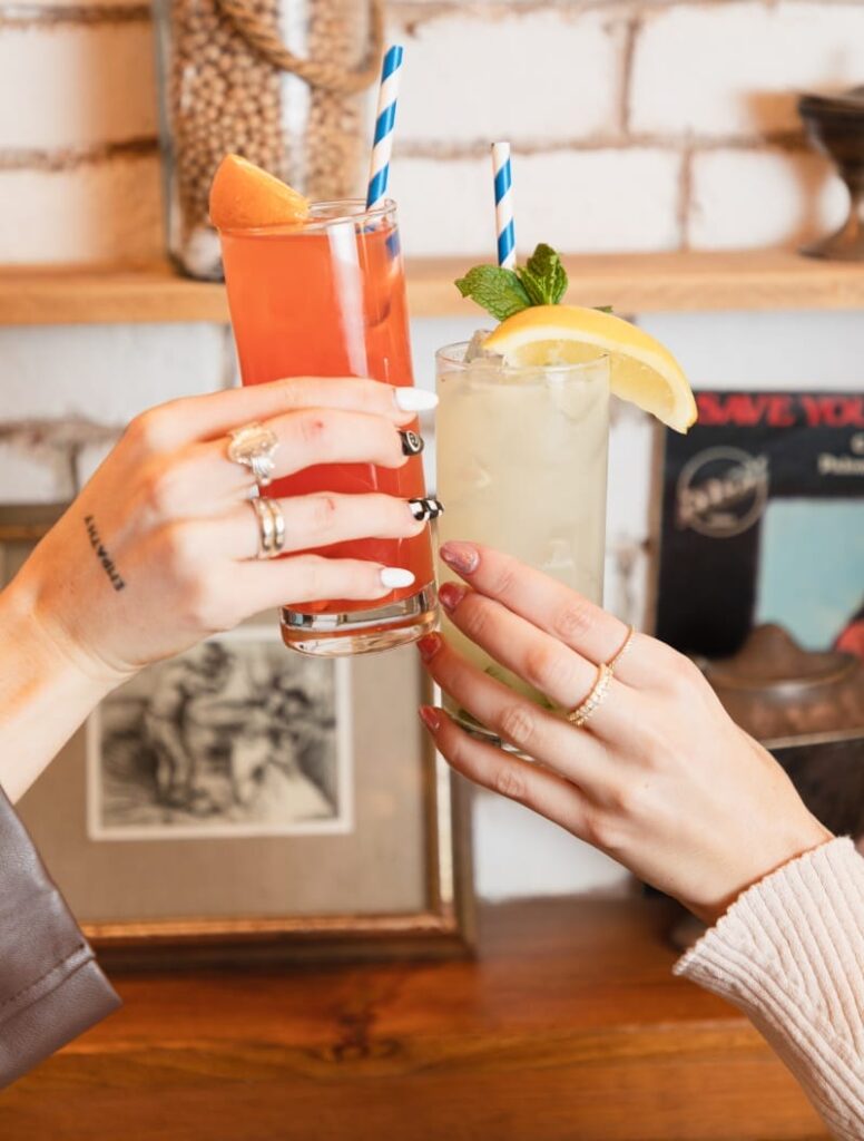 two people toasting with drinks in front of a brick wall