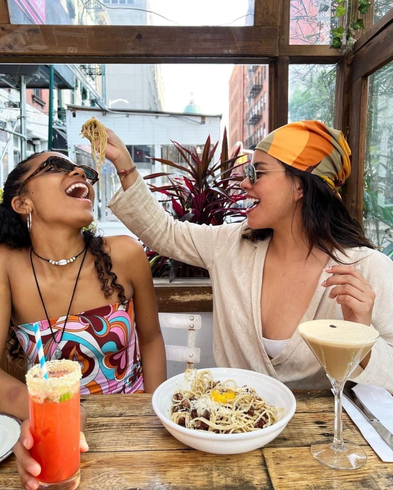 two women sitting at a table with drinks and food in front of them