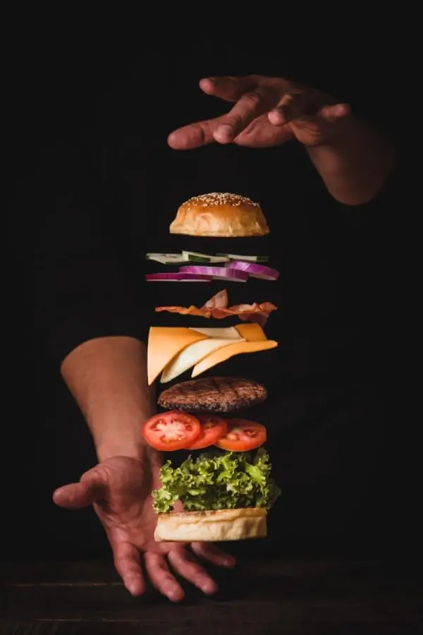 a person reaching for a hamburger with a lot of toppings
