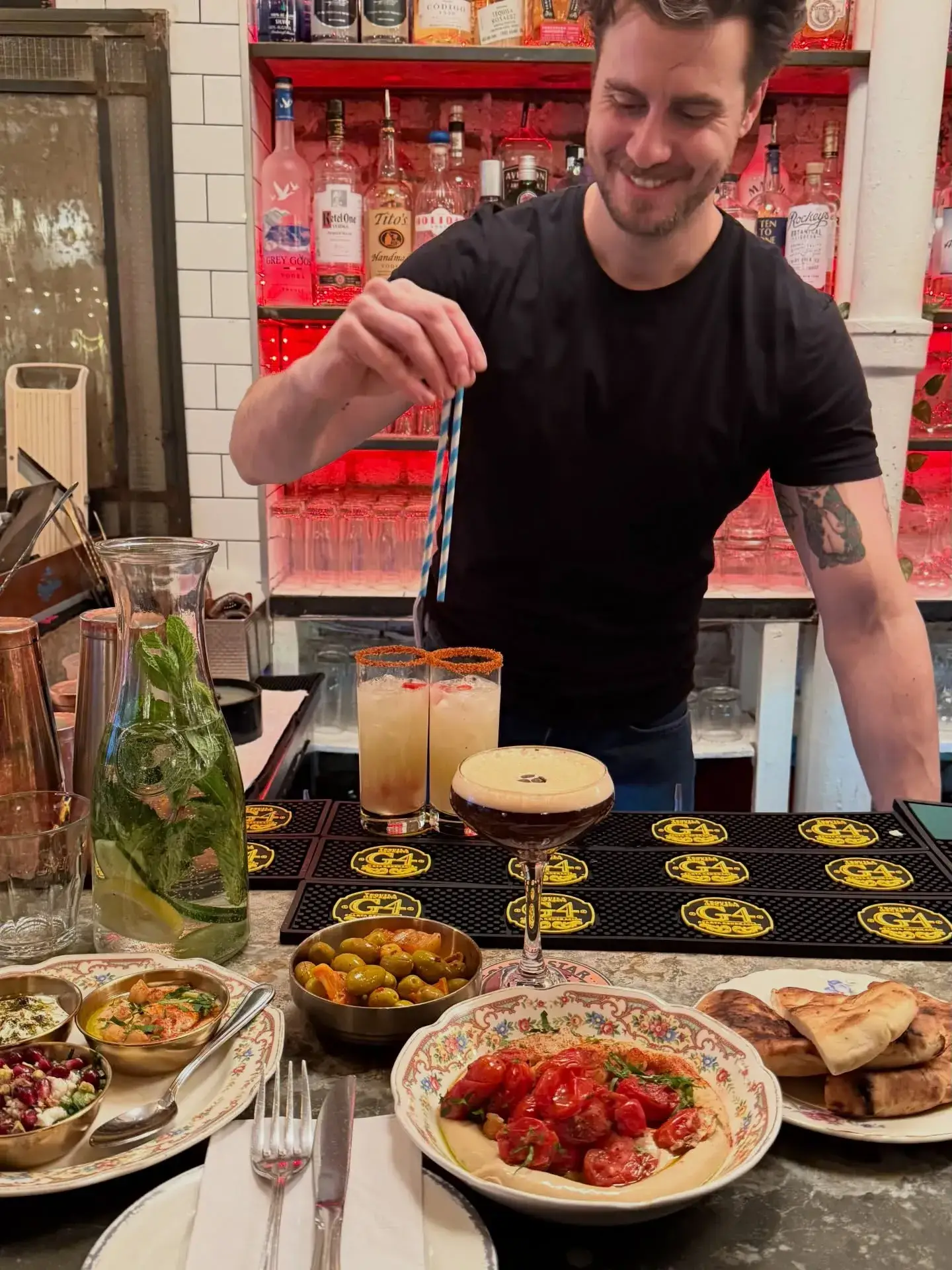 Bartender stirring cocktails beside shared plates at 19 Cleveland