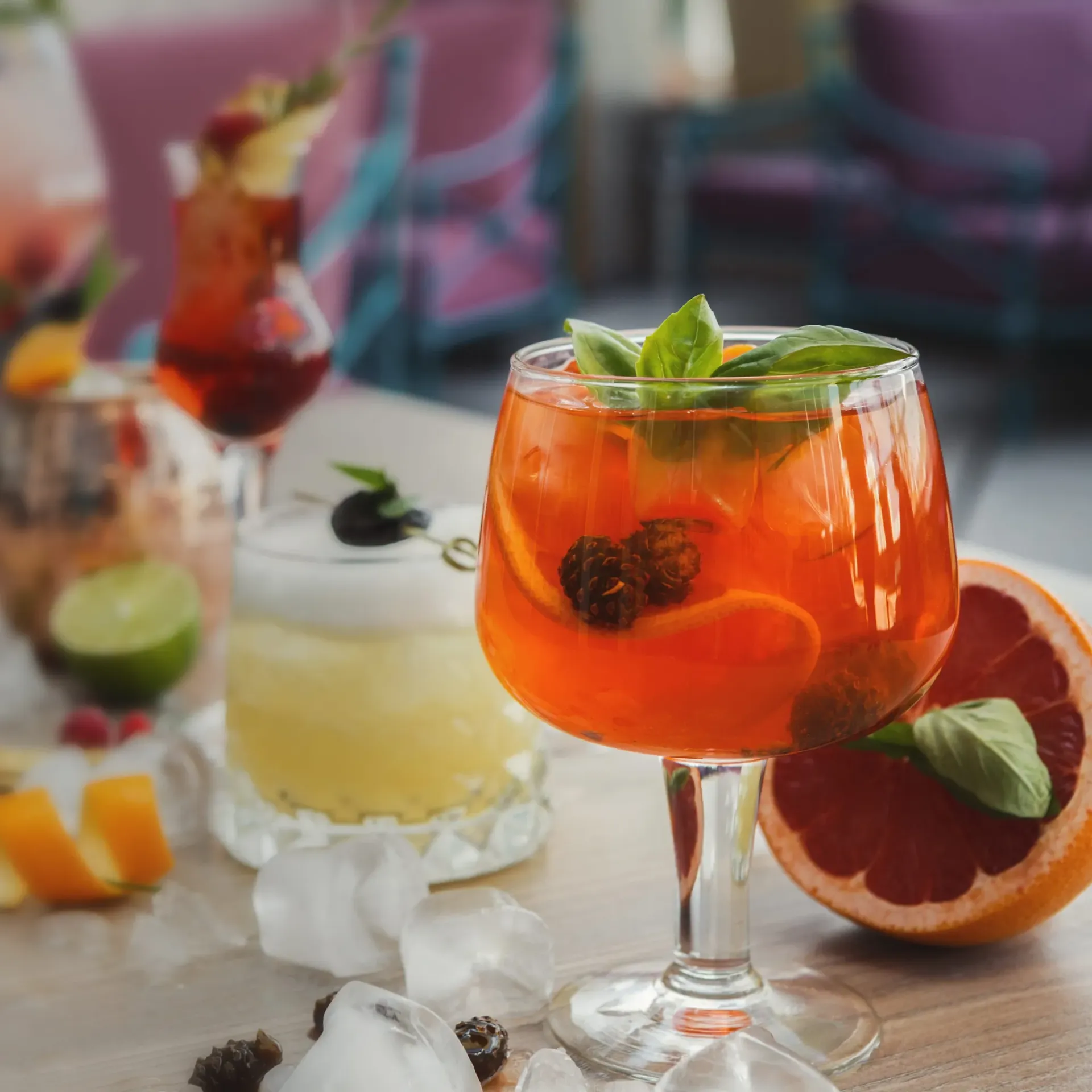 Aperol spritz cocktail with basil garnish and citrus slices on wooden table.