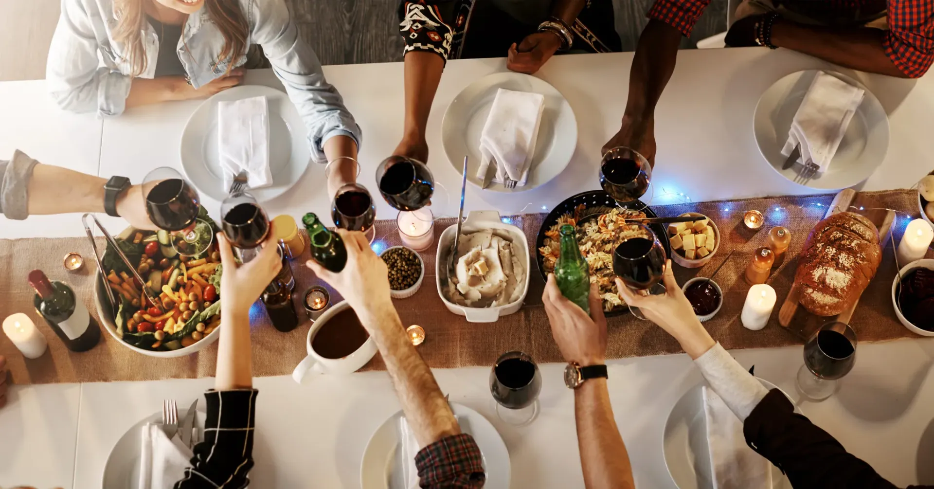 A group of people toasting with wine glasses at a dinner table filled with food and drinks.